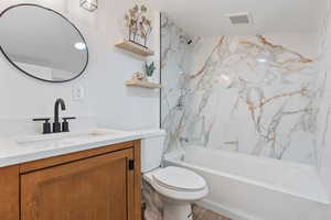 Full bathroom with tiled shower / bath, vanity, and toilet