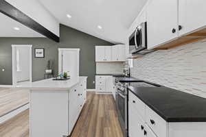 Kitchen featuring appliances with stainless steel finishes, lofted ceiling, sink, white cabinets, and a center island