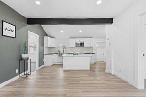 Kitchen featuring lofted ceiling with beams, light hardwood / wood-style floors, white cabinets, a kitchen island, and decorative backsplash