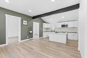 Kitchen with lofted ceiling with beams, white cabinetry, tasteful backsplash, sink, and a center island