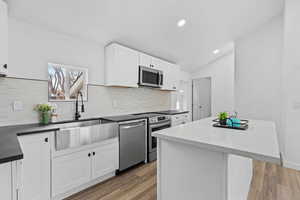 Kitchen featuring vaulted ceiling, appliances with stainless steel finishes, white cabinetry, wood-type flooring, and a center island