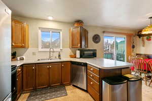 Kitchen featuring sink, hanging light fixtures, light tile patterned floors, kitchen peninsula, and black appliances