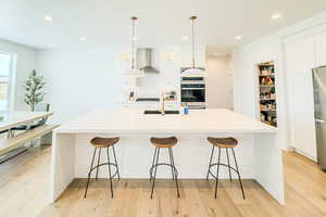 Kitchen with wall chimney range hood, stainless steel appliances, white cabinets, and a large island with sink