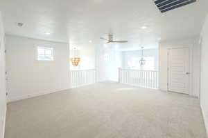 Carpeted spare room with ceiling fan with notable chandelier and a textured ceiling