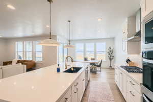 Kitchen with decorative light fixtures, appliances with stainless steel finishes, wall chimney exhaust hood, and a center island with sink