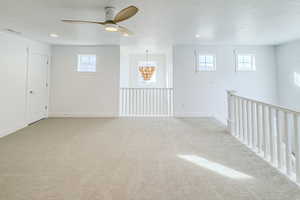 Empty room featuring a wealth of natural light, ceiling fan with notable chandelier, light carpet, and a textured ceiling