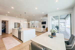 Kitchen featuring white cabinetry, decorative light fixtures, a center island with sink, stainless steel appliances, and light hardwood / wood-style floors