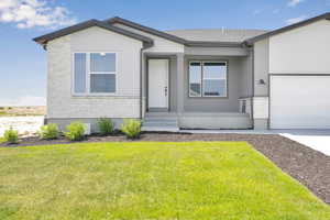 View of front of home with a garage, a front yard, stone siding, and driveway