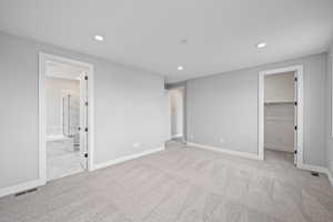 Unfurnished bedroom with ensuite bathroom, a spacious closet, light colored carpet, and a closet