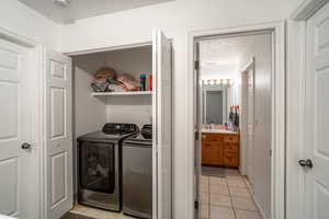 Clothes washing area featuring washer and clothes dryer, sink, a textured ceiling, and light tile patterned floors