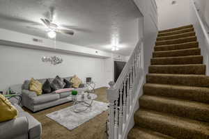 Carpeted living room featuring ceiling fan and a textured ceiling