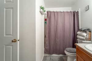 Full bathroom with vanity, shower / tub combo with curtain, a textured ceiling, and toilet