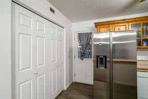 Kitchen with dark wood-type flooring, stainless steel fridge, and a textured ceiling