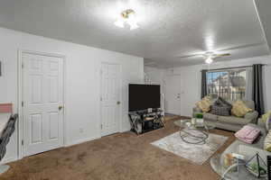 Carpeted living room featuring ceiling fan and a textured ceiling