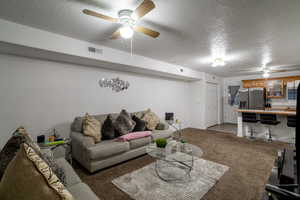 Carpeted living room featuring ceiling fan and a textured ceiling