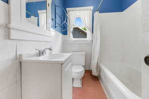 Full bathroom with vanity, toilet, shower / tub combo, and tile walls