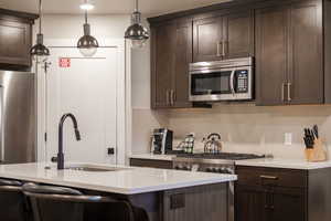 Kitchen with appliances with stainless steel finishes, pendant lighting, an island with sink, sink, and backsplash