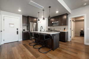 Kitchen featuring appliances with stainless steel finishes, dark hardwood / wood-style floors, pendant lighting, sink, and a center island with sink