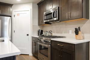 Kitchen with dark brown cabinetry, decorative backsplash, high quality appliances, and light wood-type flooring