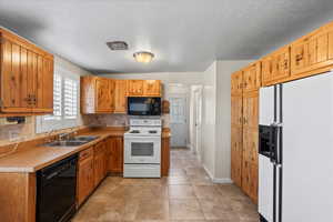 Kitchen featuring sink, backsplash, light tile patterned floors, black appliances, and a textured ceiling