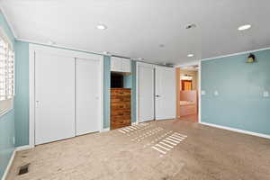 Unfurnished bedroom with light carpet, two closets, ensuite bath, and crown molding