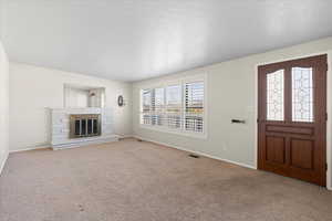 Carpeted entrance foyer featuring a fireplace and a textured ceiling