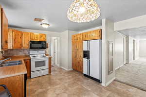 Kitchen featuring sink, backsplash, hanging light fixtures, light carpet, and white appliances