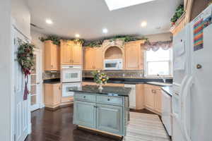 Kitchen featuring sink, a center island, light brown cabinets, white appliances, and backsplash