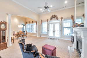 Carpeted living room featuring french doors, ornamental molding, ceiling fan with notable chandelier, and ornate columns