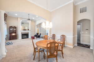 Dining room featuring light carpet, ceiling fan with notable chandelier, ornamental molding, and a high ceiling