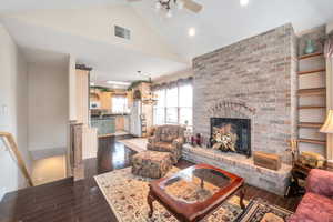 Living room featuring dark hardwood / wood-style floors, a fireplace, ceiling fan with notable chandelier, and high vaulted ceiling