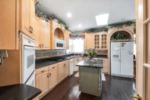 Kitchen featuring a kitchen island, light brown cabinetry, a skylight, sink, and white appliances