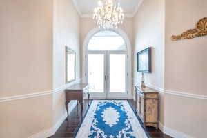 Entrance foyer featuring french doors, ornamental molding, dark hardwood / wood-style flooring, and a notable chandelier