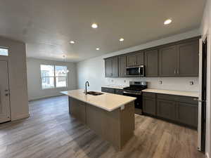 Kitchen with decorative light fixtures, sink, light hardwood / wood-style floors, stainless steel appliances, and a center island with sink