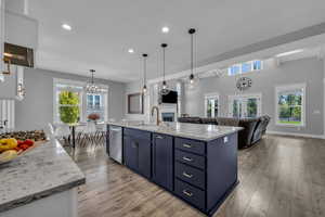 Kitchen featuring a kitchen island with sink, pendant lighting, wall ovens, white and blue cabinets, and appliances with stainless steel finishes