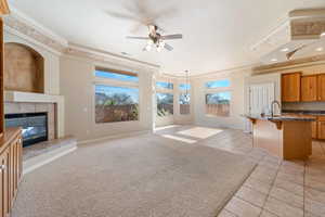 Unfurnished living room featuring crown molding, light carpet, a raised ceiling, ceiling fan, and a tiled fireplace