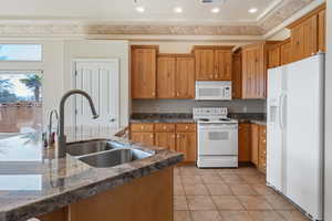 Kitchen featuring sink, white appliances, dark stone counters, and light tile patterned flooring