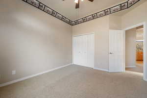 Unfurnished bedroom with a high ceiling, a closet, ceiling fan, and carpet flooring