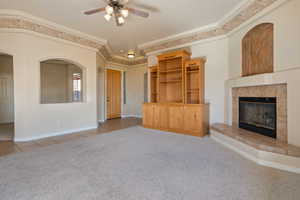 Unfurnished living room featuring light carpet, crown molding, a fireplace, and ceiling fan