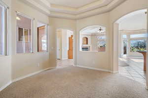 Carpeted empty room with a raised ceiling, ceiling fan, and a high ceiling