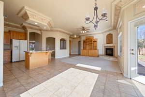 Kitchen featuring light tile patterned flooring, a tile fireplace, hanging light fixtures, ornamental molding, and white refrigerator with ice dispenser