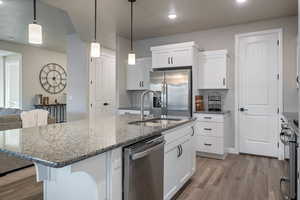 Kitchen featuring pendant lighting, sink, dark stone countertops, stainless steel appliances, and white cabinets