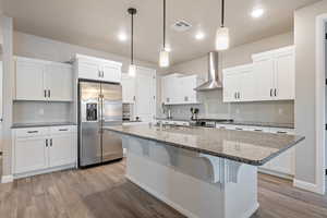 Kitchen featuring white cabinetry, pendant lighting, stainless steel fridge, and wall chimney range hood