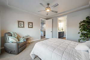 Bedroom with light carpet, connected bathroom, a raised ceiling, and ceiling fan