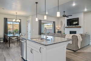 Kitchen featuring sink, white cabinetry, a kitchen island with sink, light stone countertops, and decorative light fixtures