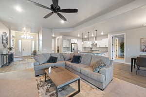 Living room featuring ceiling fan with notable chandelier and light wood-type flooring