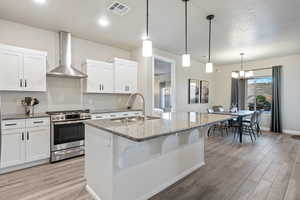 Kitchen featuring wall chimney exhaust hood, stainless steel range with gas stovetop, sink, and white cabinets