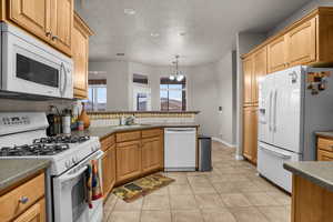 Kitchen with light tile patterned flooring, sink, tasteful backsplash, pendant lighting, and white appliances