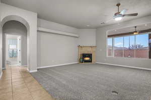 Unfurnished living room featuring ceiling fan, light tile patterned floors, a textured ceiling, and a fireplace