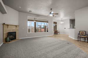 Unfurnished living room featuring ceiling fan, a tiled fireplace, a textured ceiling, and light tile patterned floors